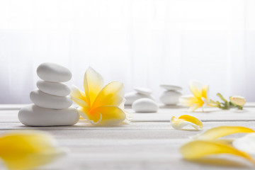 Fototapeta na wymiar Stacked white stones on white background with yellow frangapani flower - Lifestyle and alternative health concept image with copy space for text.