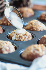 Fresh from the oven, homemade pumpkin muffins with streusel with spoon pouring icing over them. Selective focus on center muffin with extreme blurred foreground and background.