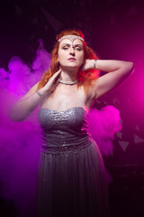 Fototapeta premium Mature plus size red hair woman in grey evening dress posing on dark smoke background ready for halloween.