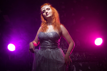 Fototapeta premium Mature plus size red hair woman in grey evening dress posing on dark smoke background ready for halloween.