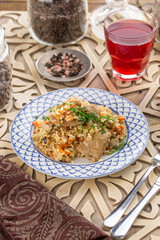 pilaf with chicken on white plate and glass of red drink on oriental wooden table