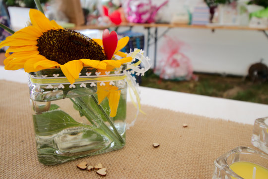 Wedding decoration with a sunflower and a red heart in a glass plus a candle an little wooden hearts. Gift table in the background