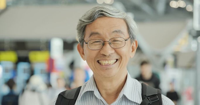 Portrait of senior man smiling at the flight timetable background in airport.