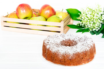 Apple Bundt Cake Sprinkled with Icing Sugar on white old wooden table with apples and spring bouquet