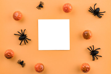 Creative Halloween composition. Pumpkins, spiders and paper blank on pastel orange background. Flat lay, top view, copy space