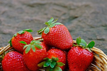 Strawberries in basket with stone as background.
