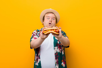 young big size man with a hot dog against flat wall