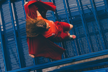 Young woman in red mantle run on blue stairs. Millennial concept.