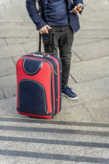 Unrecognizable young man traveling in the street with suitcase and using smartphone navigating system at city street, travel and tourism concept
