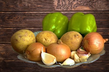 fresh vegetables, onions, garlic, potatoes and green paprika in a plate on a wooden background