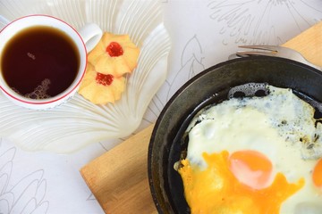 breakfast on the table, scrambled eggs in a cast iron skillet, tea in a mug and cookies on a saucer