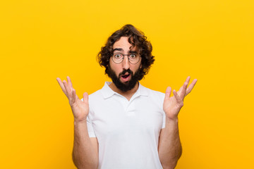 young crazy man looking shocked and astonished, with jaw dropped in surprise when realizing something unbelievable against yellow wall - obrazy, fototapety, plakaty