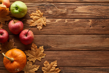 top view of small pumpkin and apples on brown wooden surface with dried autumn leaves