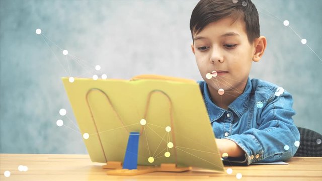 Young concentrated school kid in blue jeans t-shirt writing, copying the text from book on the bookholder.