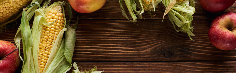 panoramic shot of fresh apples and sweet corn on brown wooden surface with copy space