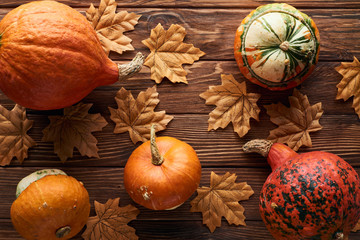 top view of ripe pumpkins on brown wooden surface with dry autumn leaves