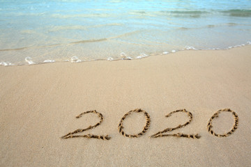 Year 2020 written at the caribbean sand beach with sea wave .