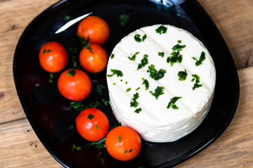 Breakfast food, cheese and cherry tomatoes on dish, on a rustic wooden plank board table background.