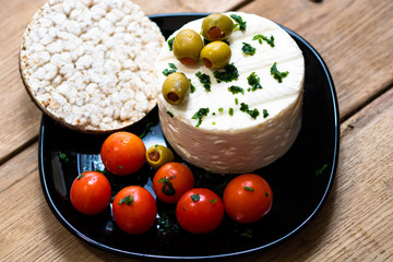 Breakfast dish (cheese, meatballs, green olives, cherry tomatoes, rice crackers) on a rustic wooden plank board table background.