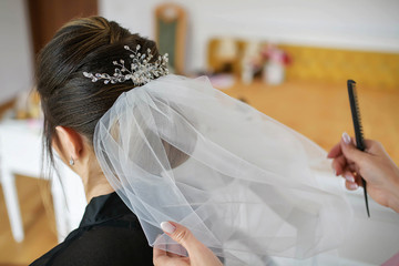 Young Caucasian bride getting her hair done for her wedding day. Hair stylist working on a woman's dark hair, setting a tulle veil in a sophisticated coiffure using bobby pins and a fine-toothed comb © Ana