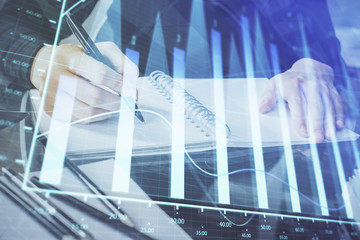 Forex chart hologram on hand taking notes background. Concept of analysis. Multi exposure