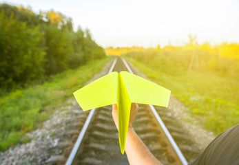 Guy is holding yellow handmade paper plane. Freedom concept photo with rail tracks. Travel lifestyle motivation. Railway transport industry.