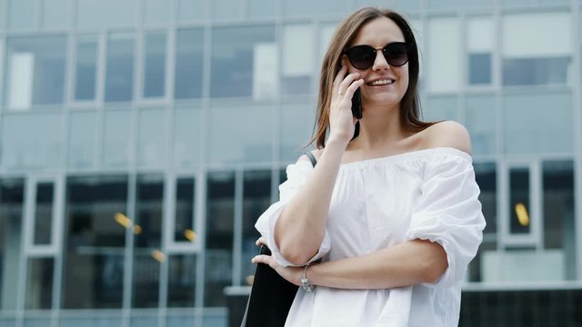 Modern and happy young businesswoman speak by mobile phone and smiling, business center in the background