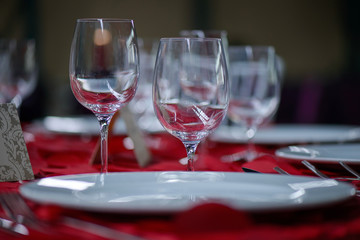 Fine dining table setting with white china and wine and water crystal glasses, with silverware in the order of use, and romantic red tablecloth ready for guests at an event, wedding or at a restaurant