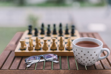 Obraz na płótnie Canvas Close up photo of glasses, white cup of black tea and chess on wooden table. Chess pieces ready for the game.Cozy evenings, home atmosphere. Concept of comfort and coziness. Autumn mood. Side view.