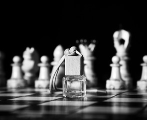 Small bottle of perfume is on chessboard as a chess piece. First move has done with fragrance.