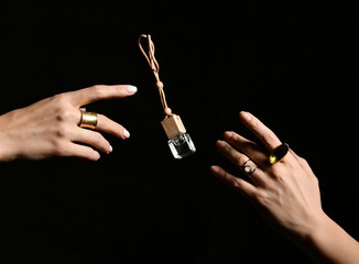 Small perfume bottle is flying from one pretty woman hand to another on black background