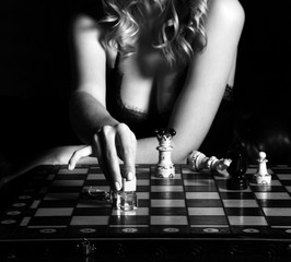 Seductive woman in lace lingerie with deep neckline playing chess with perfume bottles, pointing one