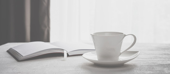 cup of coffee, a plaid notebook on the table in front of a window with a copy space
