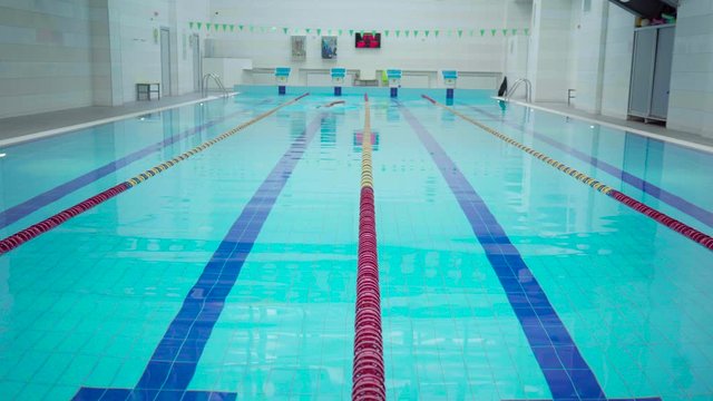 Professional skill male swimmer in indoor pool swimming across track. Healthy lifestyle. Sports and recreation.