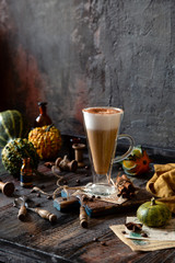 autumn traditional hot drink pumpkin spice latte in glass cup with foamy whipped cream on rustic wooden table with cinnamon, spoons and assorted mini pumpkins