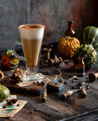 autumn traditional hot drink pumpkin spice latte in glass cup with foamy whipped cream on rustic wooden table with cinnamon, spoons and assorted mini pumpkins
