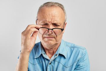 Vision problems. An elderly man takes off his glasses. Not satisfied. Senior citizen on a white...