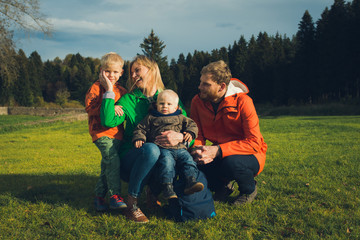 Fototapeta premium happy family in autumn forest sitting on grass - loving parents and sons
