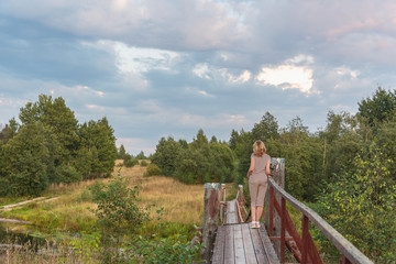 A girl is standing on a suspension bridge across a forest river