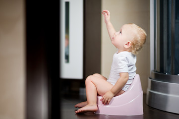 baby sits on a piss-pot in the bathroom and pulls her hand up