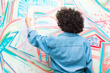 young pretty afro woman standing and pointing to object on copy space, rear view against graffiti wall
