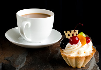 Fruit cake with cherries, grapes and plum stands on a wild stone next to a white cup of coffee with a foam