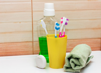 toothbrushes in yellow glass, dental floss and mouthwash and towel