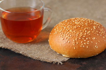 Tea in a glass mug and a sesame bun on burlap tablecloth.