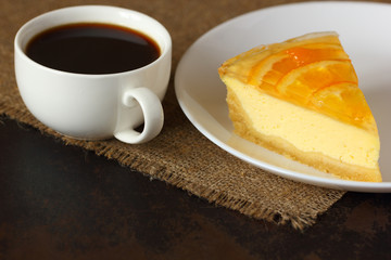 Cheesecake with oranges and a mug of coffee on burlap tablecloth.