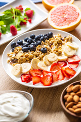 Healthy breakfast served with plate of yogurt muesli blueberries strawberries and banana.