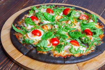 Pizza on black dough with arugula and cherry
