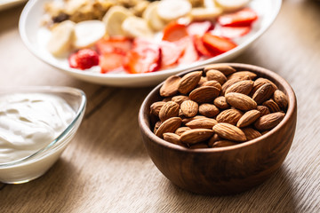 Almonds in wooden bowl with yoguth and plate of healthy breakfast