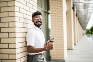 Portrait of a young handsome Indian man texting in an urban context