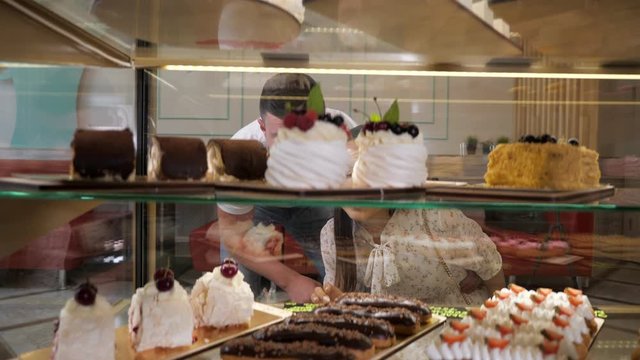 happy young couple chooses tasty fresh cakes standing in glass show case of confectionery shop close view